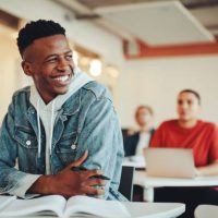 Male student sitting in university classroom looking away and smiling. Man sitting in lecture in high school classroom.